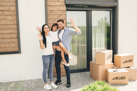 Family of three waving next to Allied van Lines moving boxes