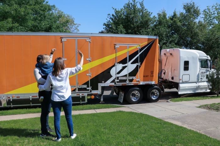 Family of three waving at Allied Van Lines moving truck