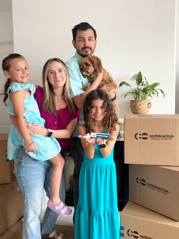 Family of four and dog standing with North American Moving Services boxes