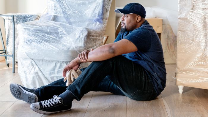Man sitting on floor with furniture wrapped up Man sitting on floor with furniture wrapped up